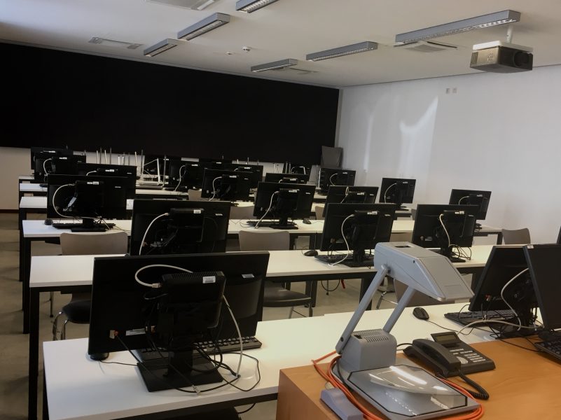 Foto: der gelcihe Seminarraum, vom Platz der Lehrperson aus fotografiert, so dass die Rückseiten der Bildschirme das Bild dominieren